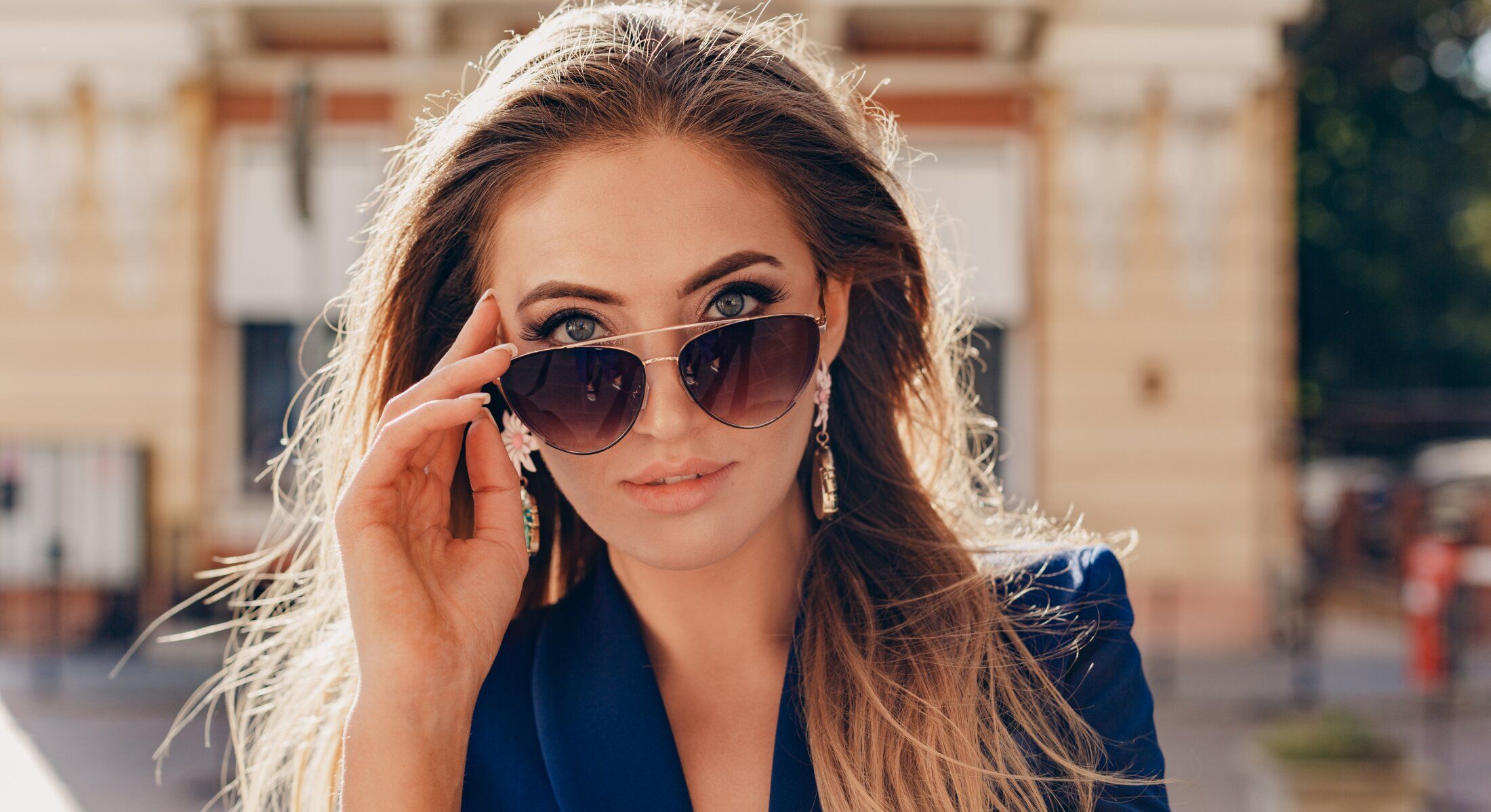 Woman in sunglasses adjusting her eyewear outdoors.
