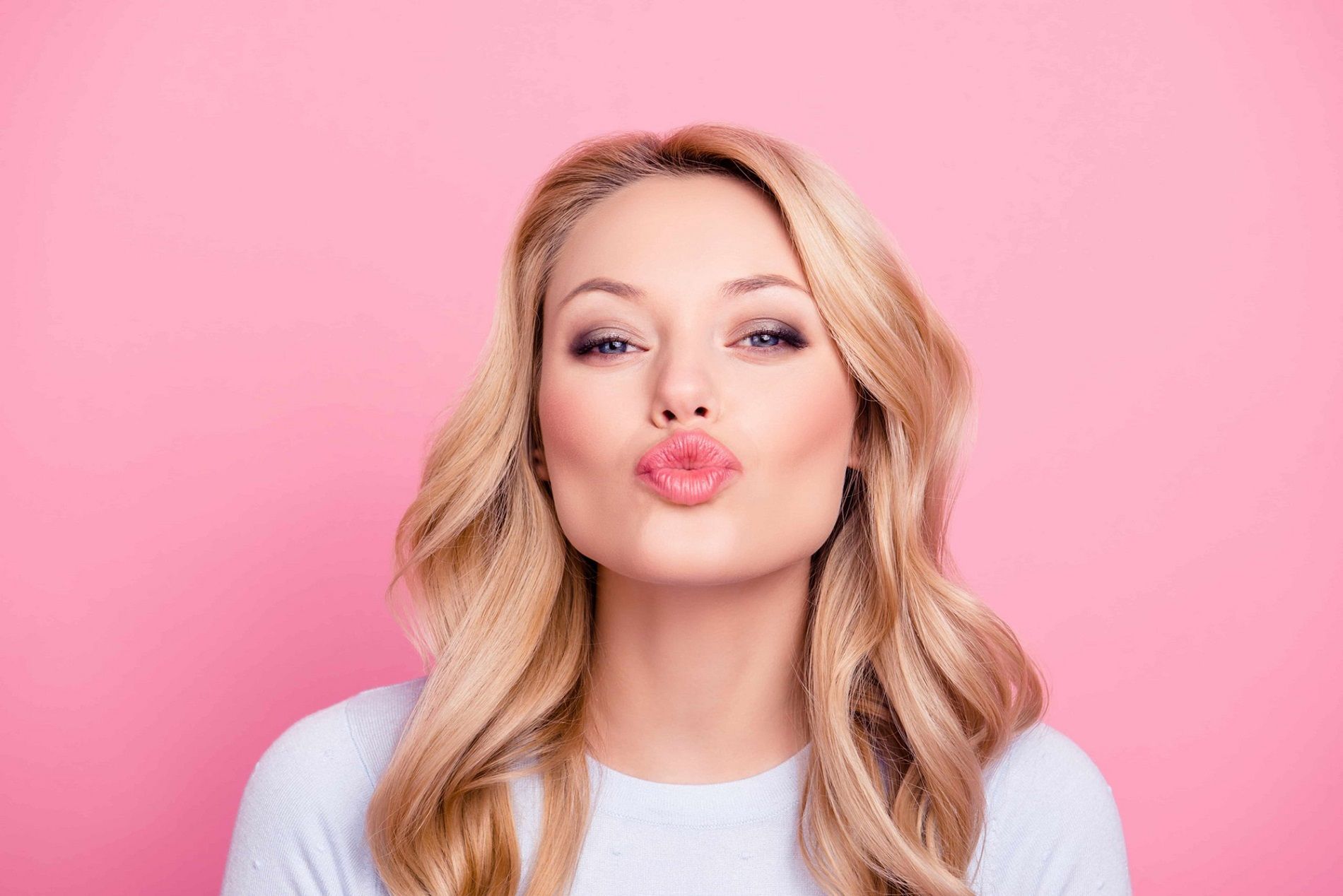 Woman blowing a kiss against pink background.